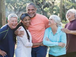 Five happy senior friends of diverse backgrounds embracing and laughing together in a sunny park setting.